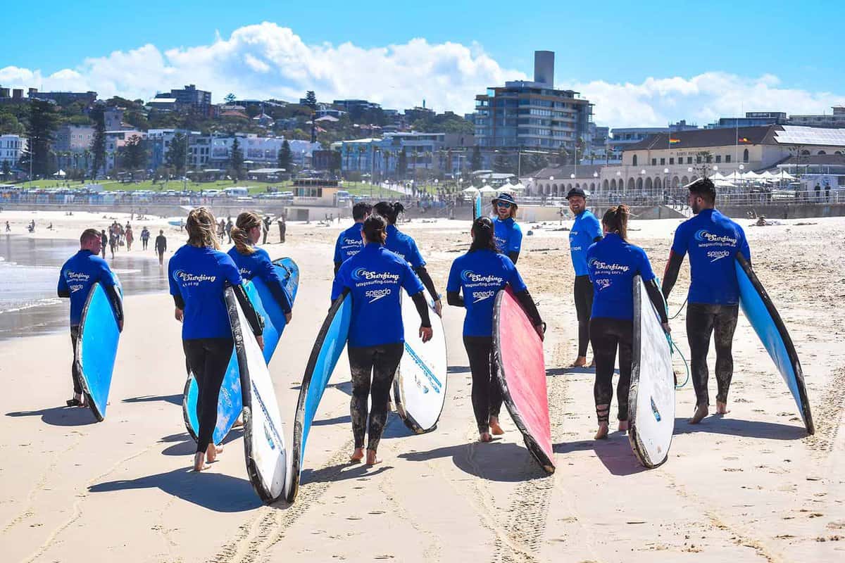 A group of people carrying surfboards along the beach.