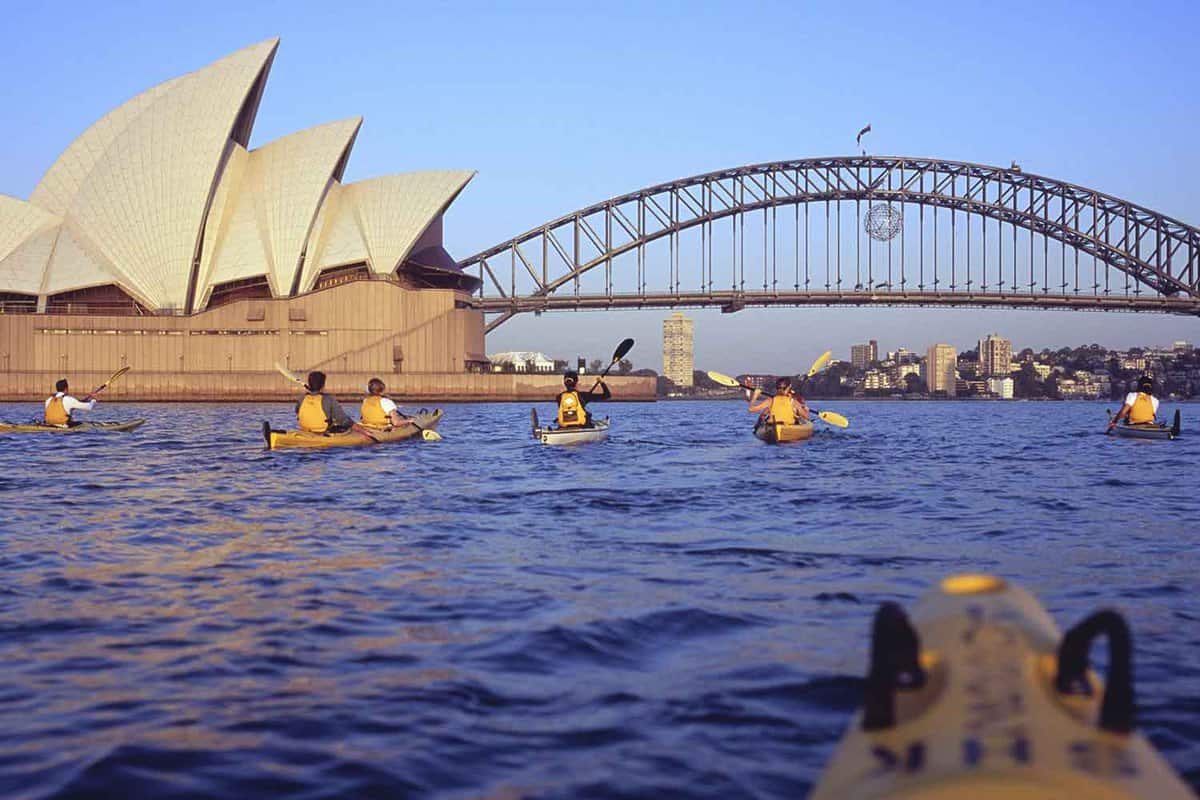 6 People kayaking in front of Sydney Harbour Bridge and the Sydney Opera House on the side. Taken by someone in a kayak.