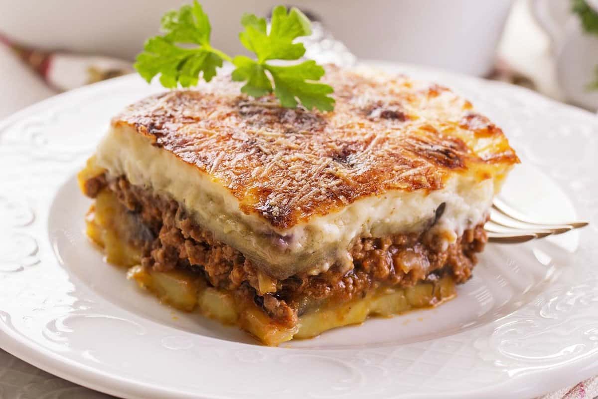 close up of a slice of Moussaka - layers of bechamel with mince topped with parsley