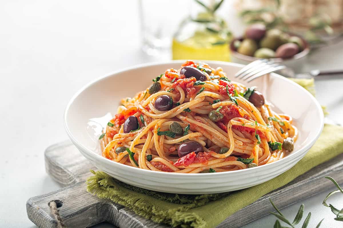 italian pasta dish with tomatoes, olives, capers and parsley. Light background. Copy space.