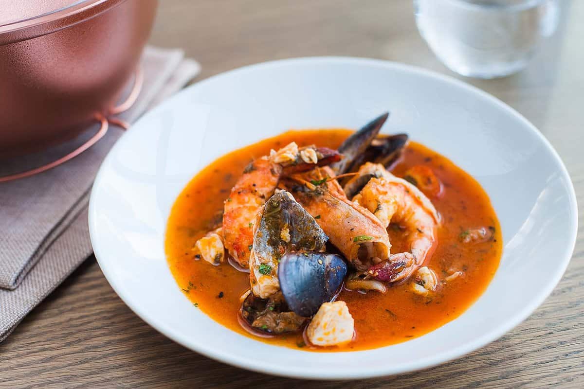 Bouillabaisse soup with shrimps, mussels and fish in a white plate on a wooden table