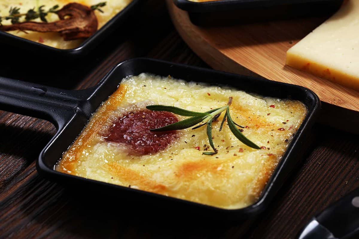Delicious traditional Swiss melted raclette cheese on diced boiled or baked potato served in individual skillets with salami.