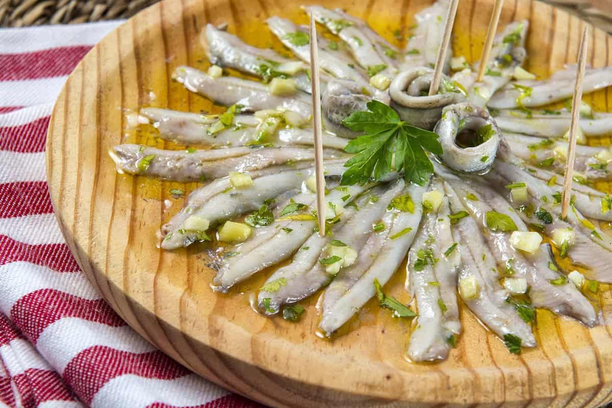 close up of a wooden platter of small fish in oil