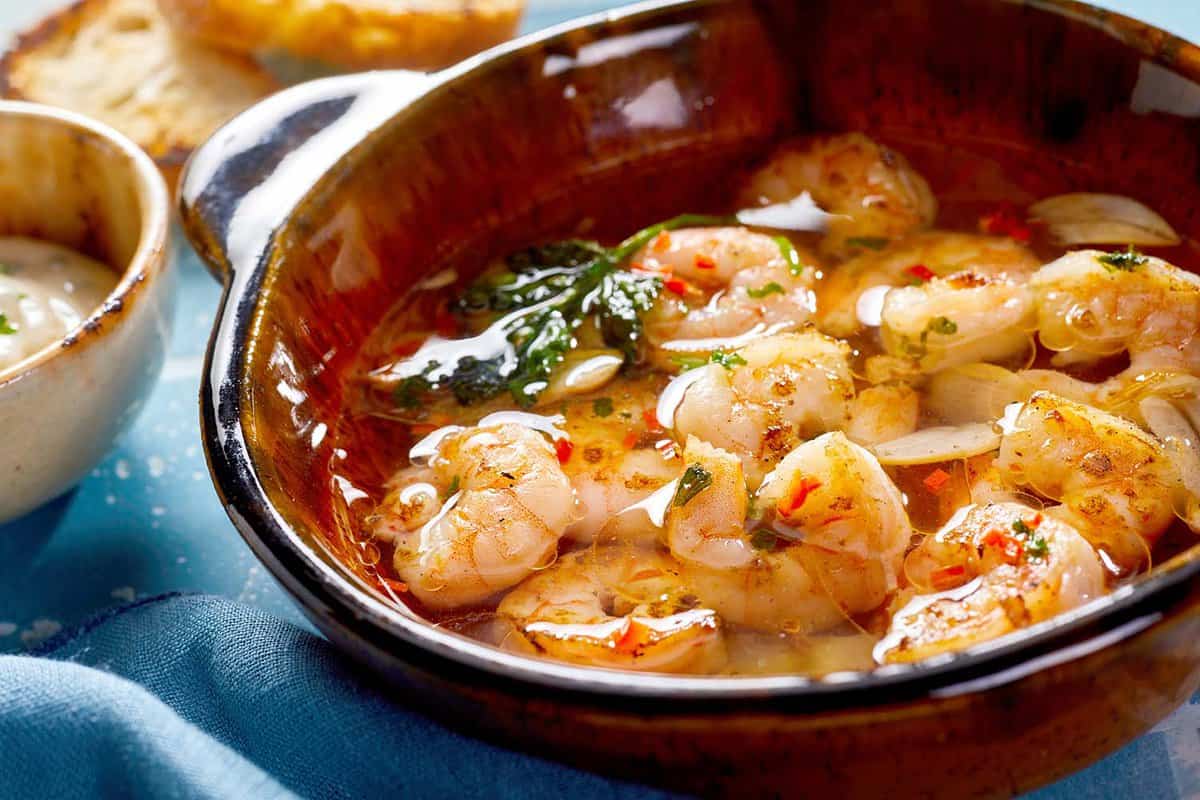 Spicy grilled fresh scampi or lobster with garlic and herbs served in a brown ceramic bowl in close up