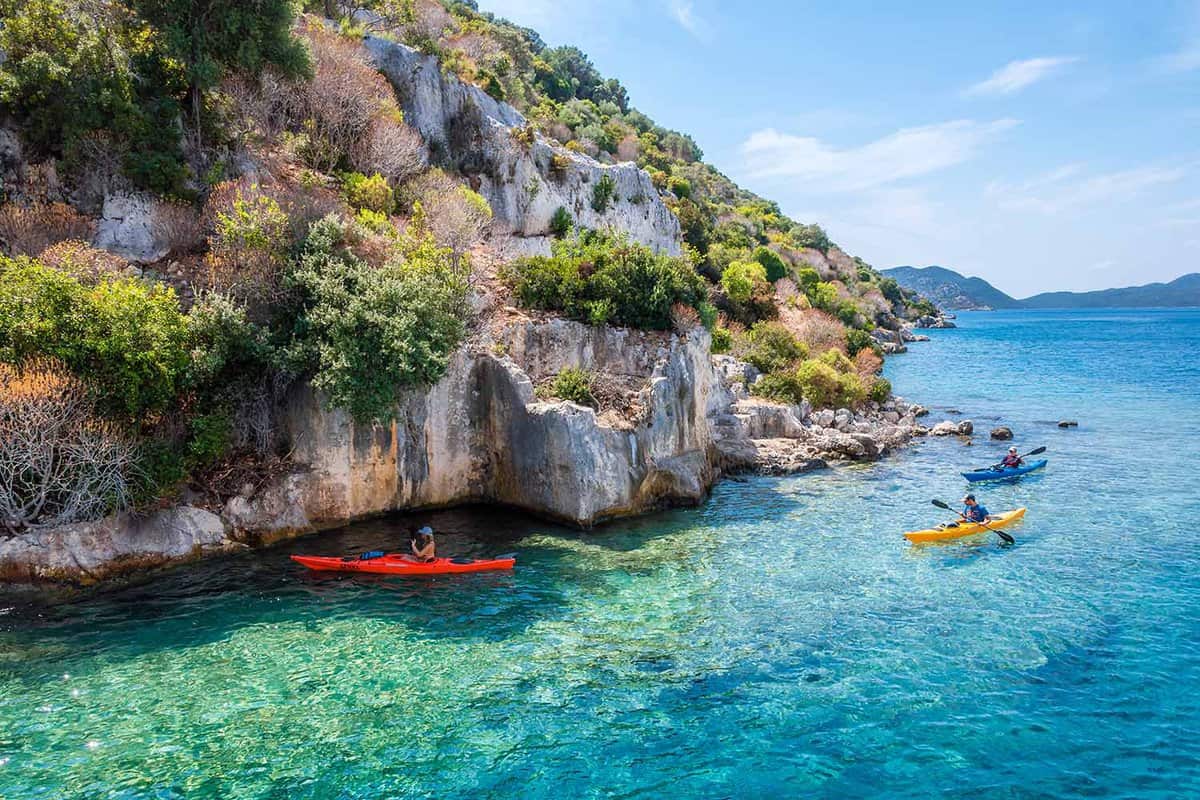 People kayaking on the water on the side of a cliff