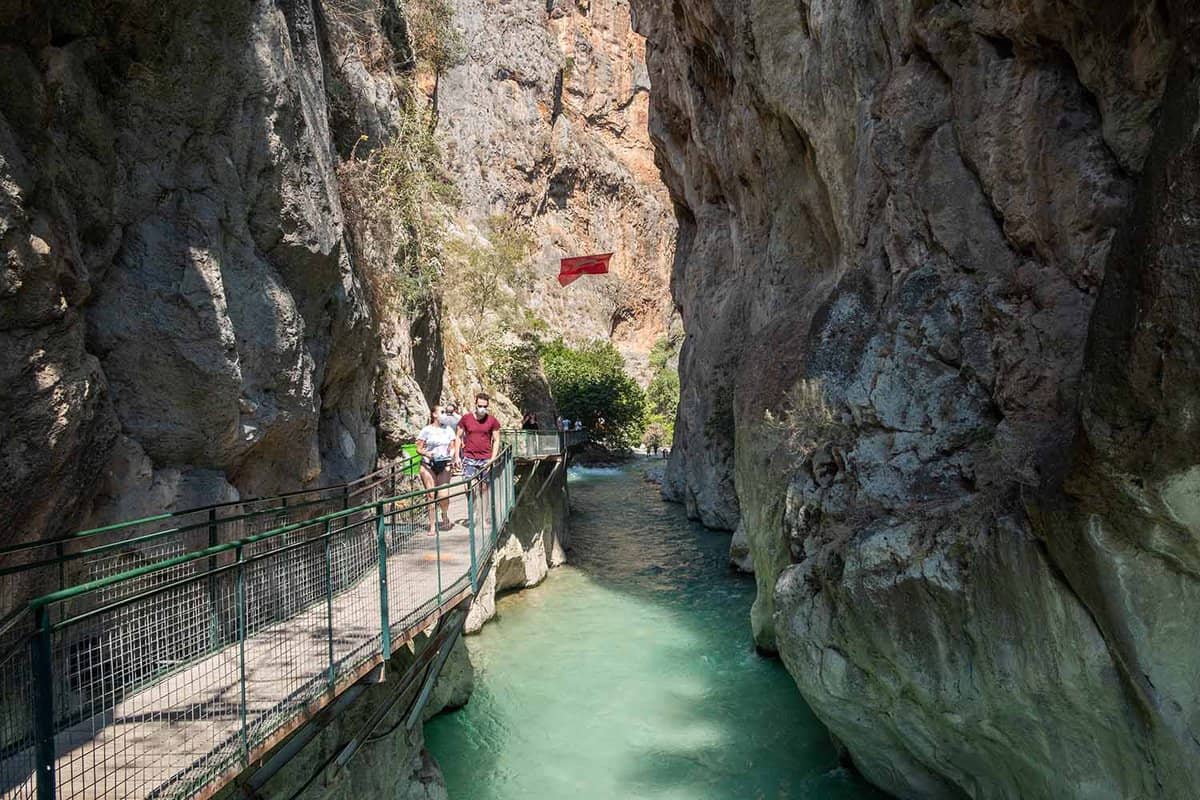 Tourists walk along a footbridge next to the stream at the bottom of the canyon