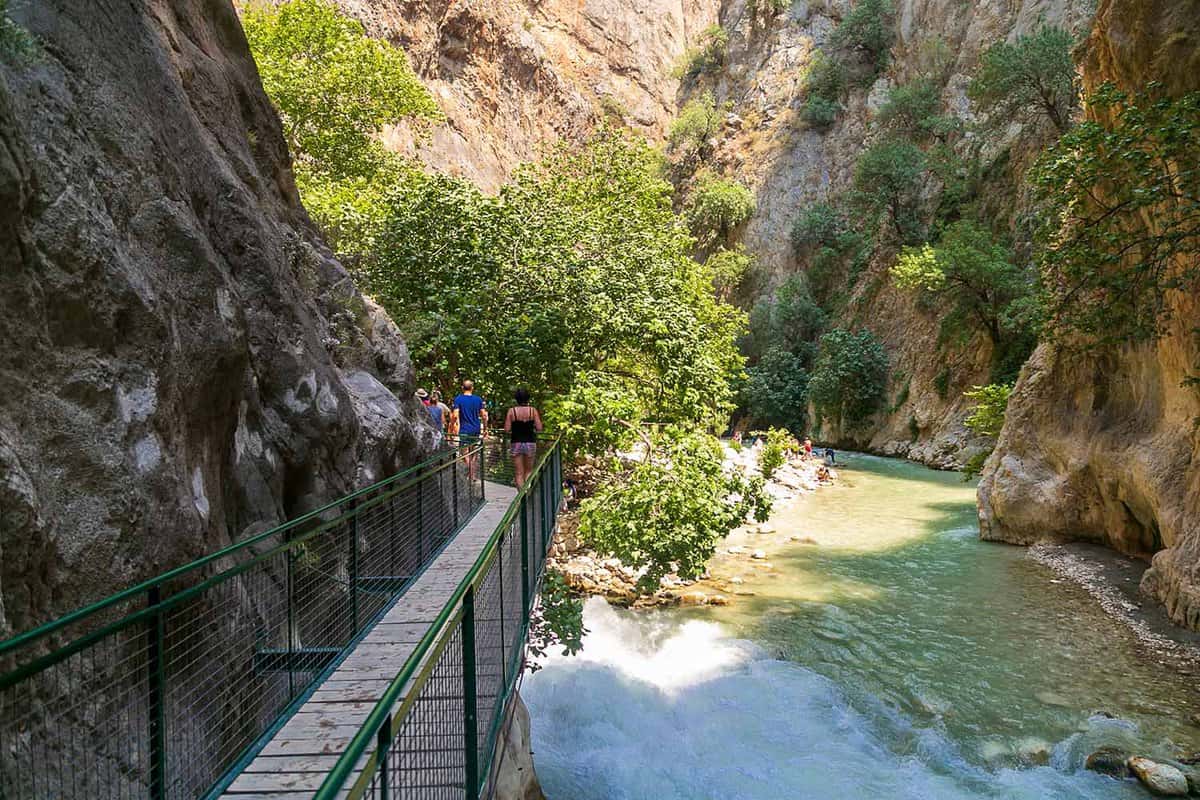 People walking along the footbridge as others are in the river at the bottom of the canyon