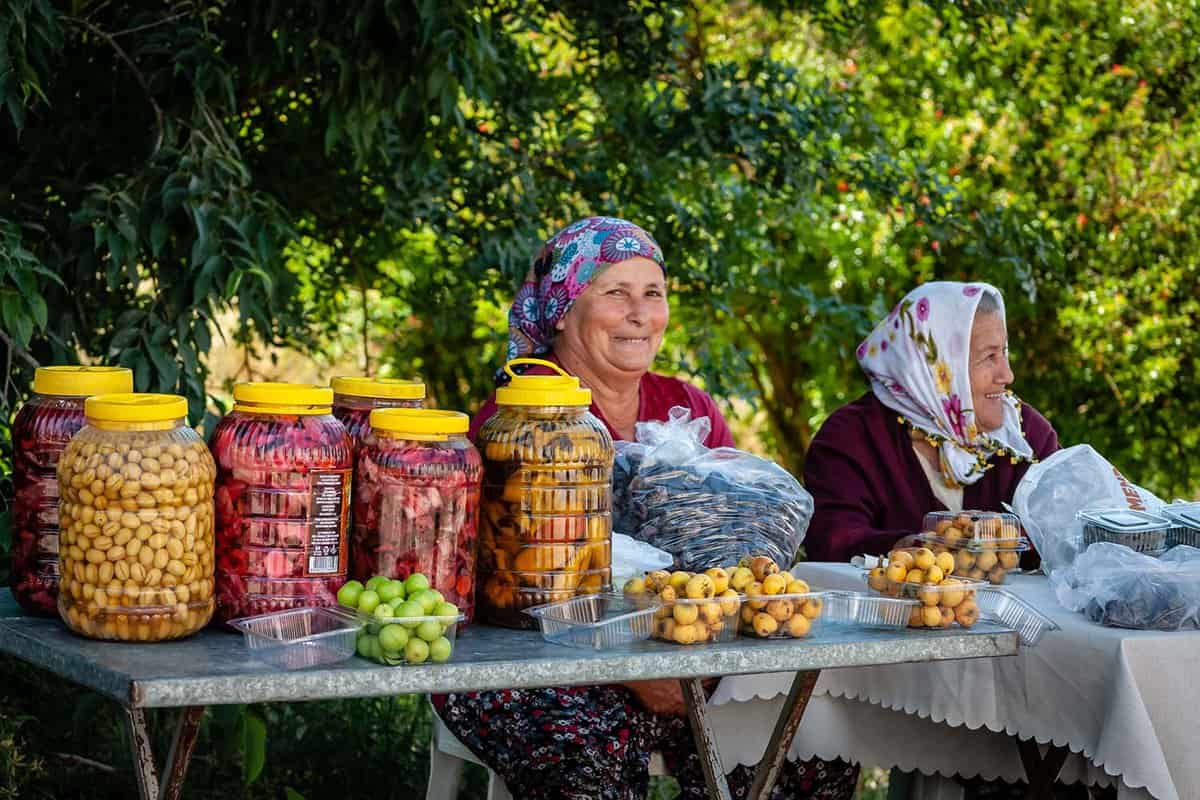Women selling jars of homemade olives, pickled vegetables, and home grown dried and fresh fruit at a local street fair