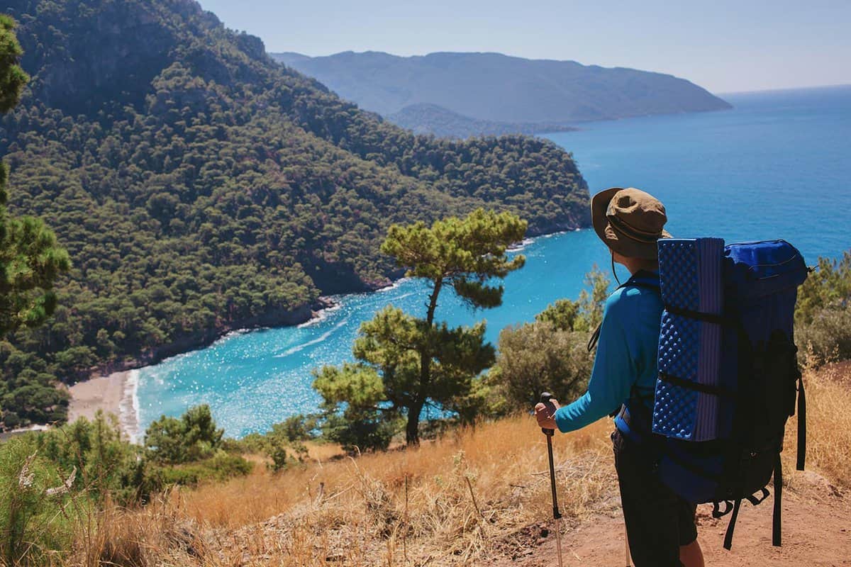 Man with backpack relaxing on top of a mountain and enjoying on view the bay of Kabak and sea landscape. Hiking travel to Turkey, lycian way