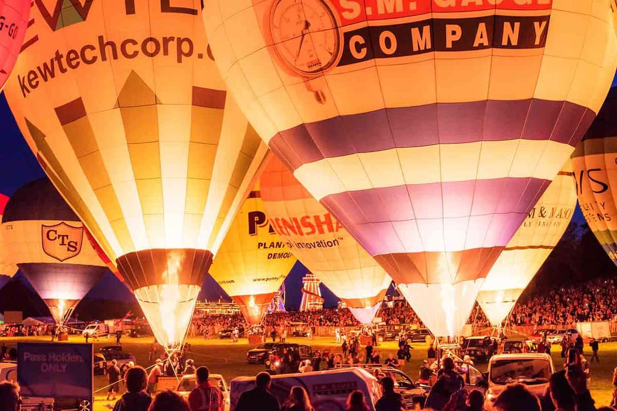8 grounded hot air balloons at night with crowds around