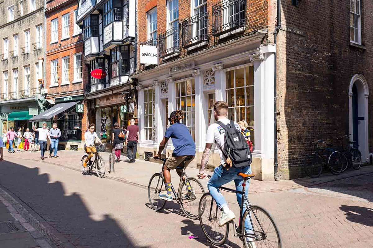 Young students cycling down a pedestrianised high street lined with shops