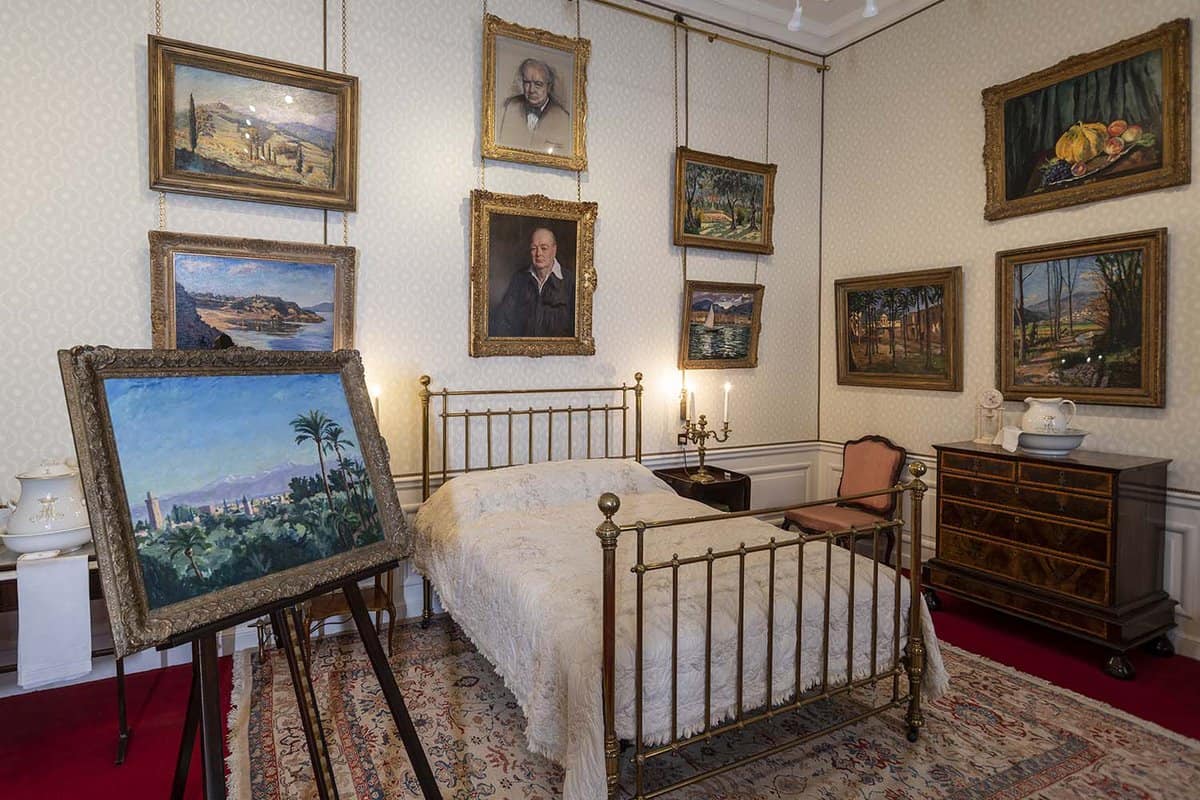 An old bed in a big room with lots of paintings.