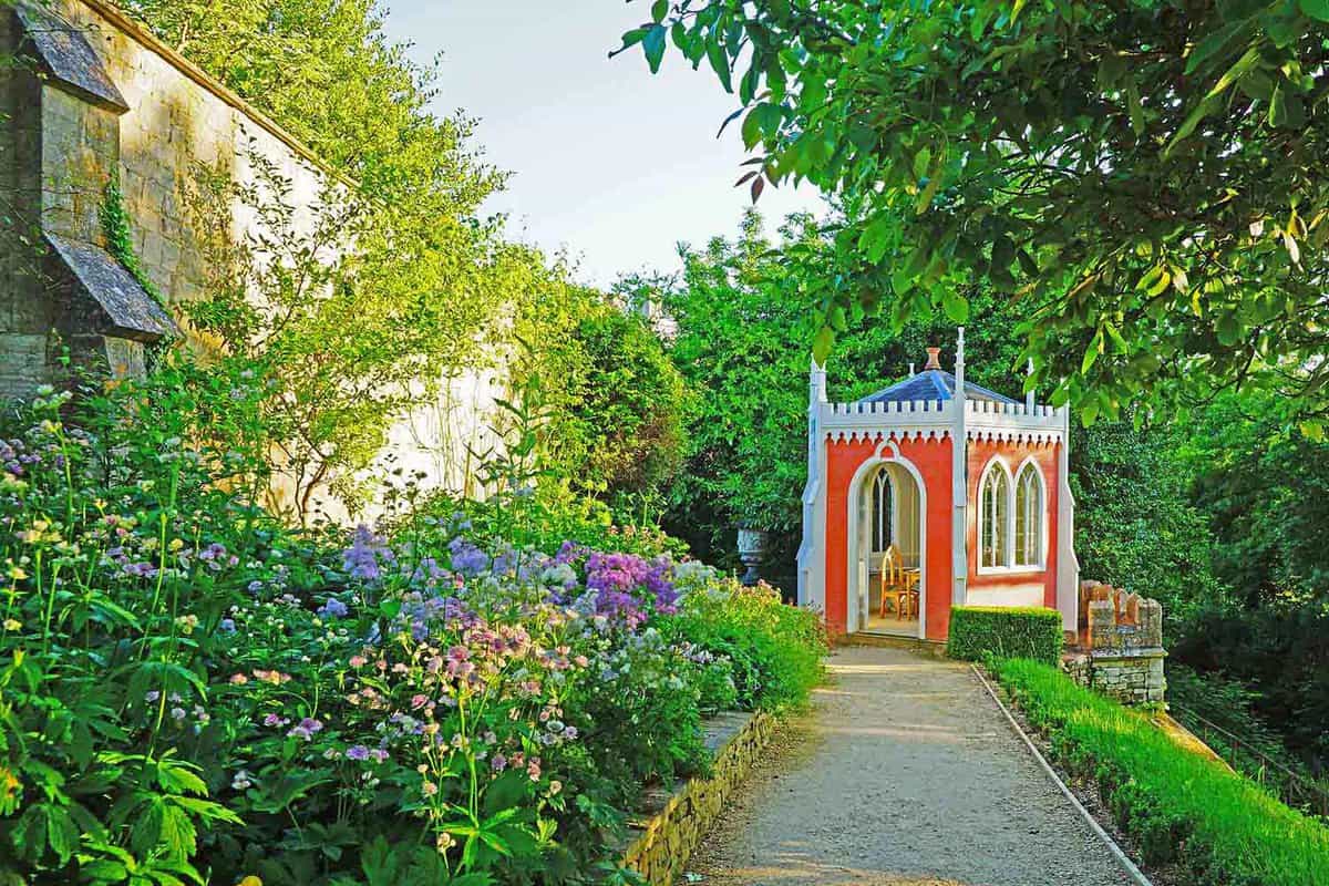 A pathway leading up to a red gazebo in a garden