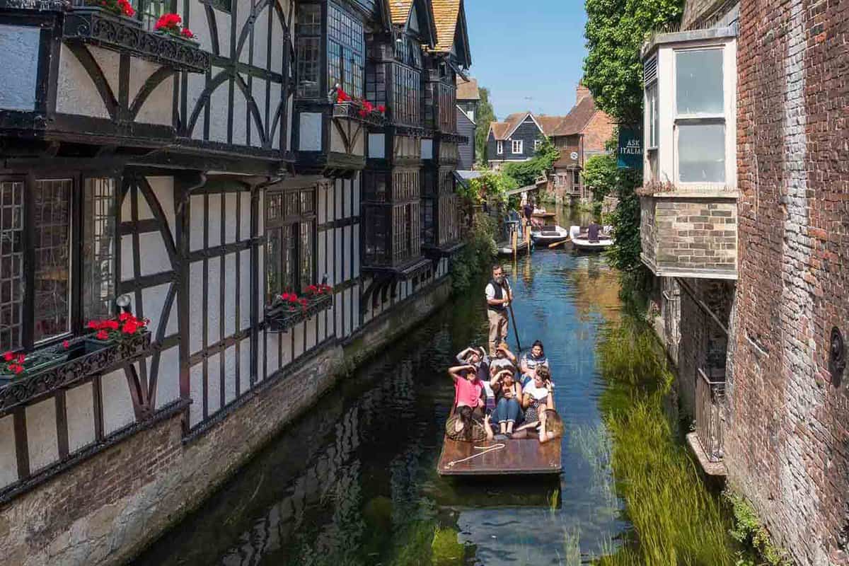 Tourists punting down narrow stretch of the River Stour lined with Tudor buildings