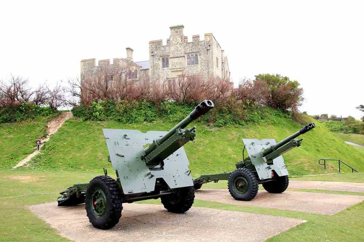 An image of a two World War 2 anti-aircraft guns at Dover Castle. The Castle itself can be seen further in the background on a slightly raised hill, amongst the clouds