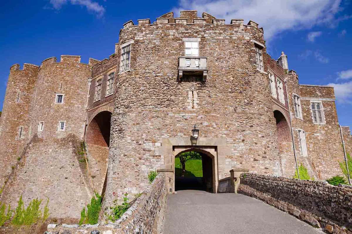 A low angle view of Dover castle, showcasing the bridge to a Medieval gateway that has a curved arch passageway through the Castle
