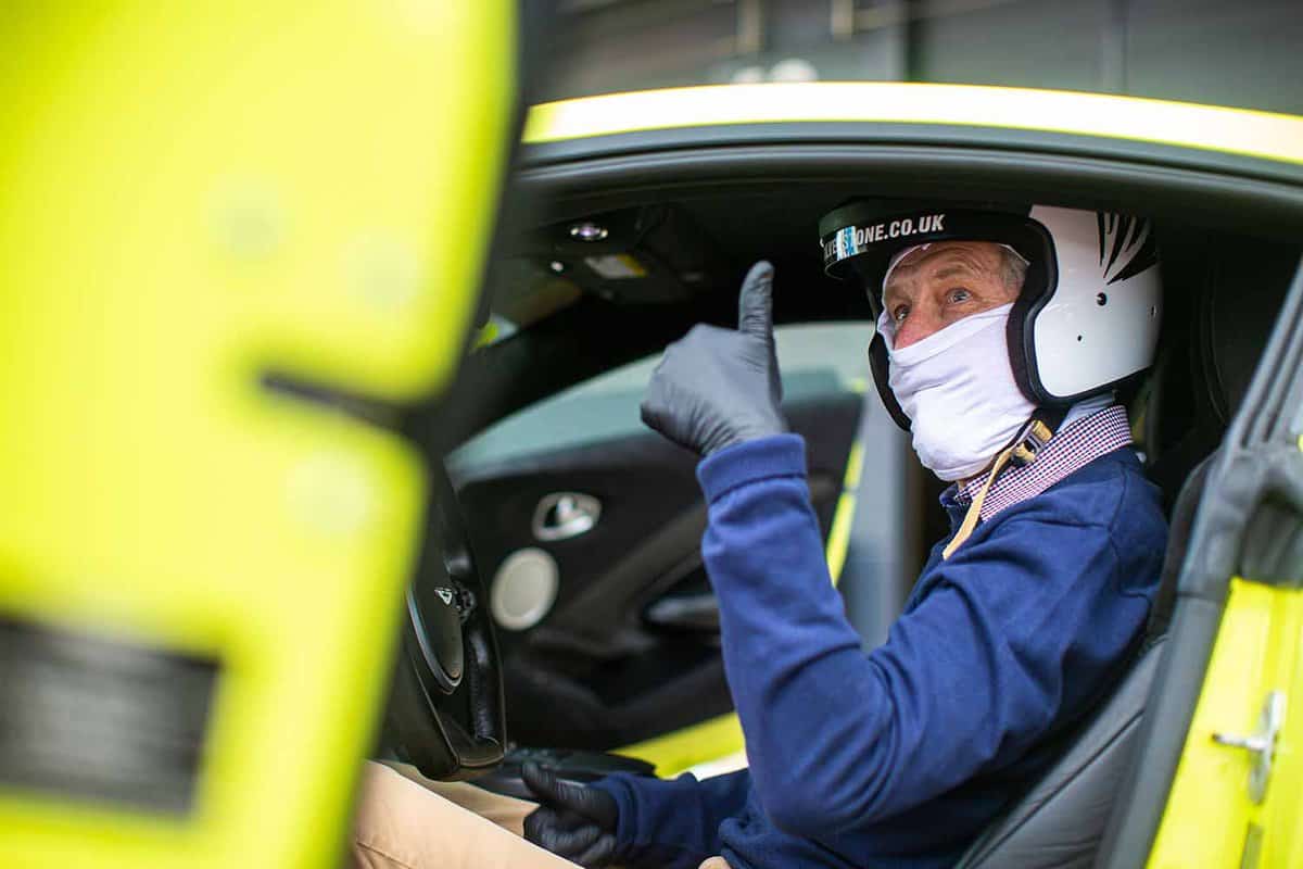 A driver inside a car, wearing a protective helmet doing a thumbs up sign