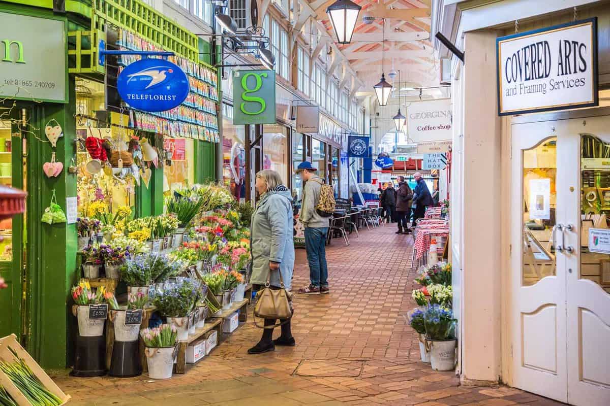 Arcade of shops with a lady looking at a flwoer stall