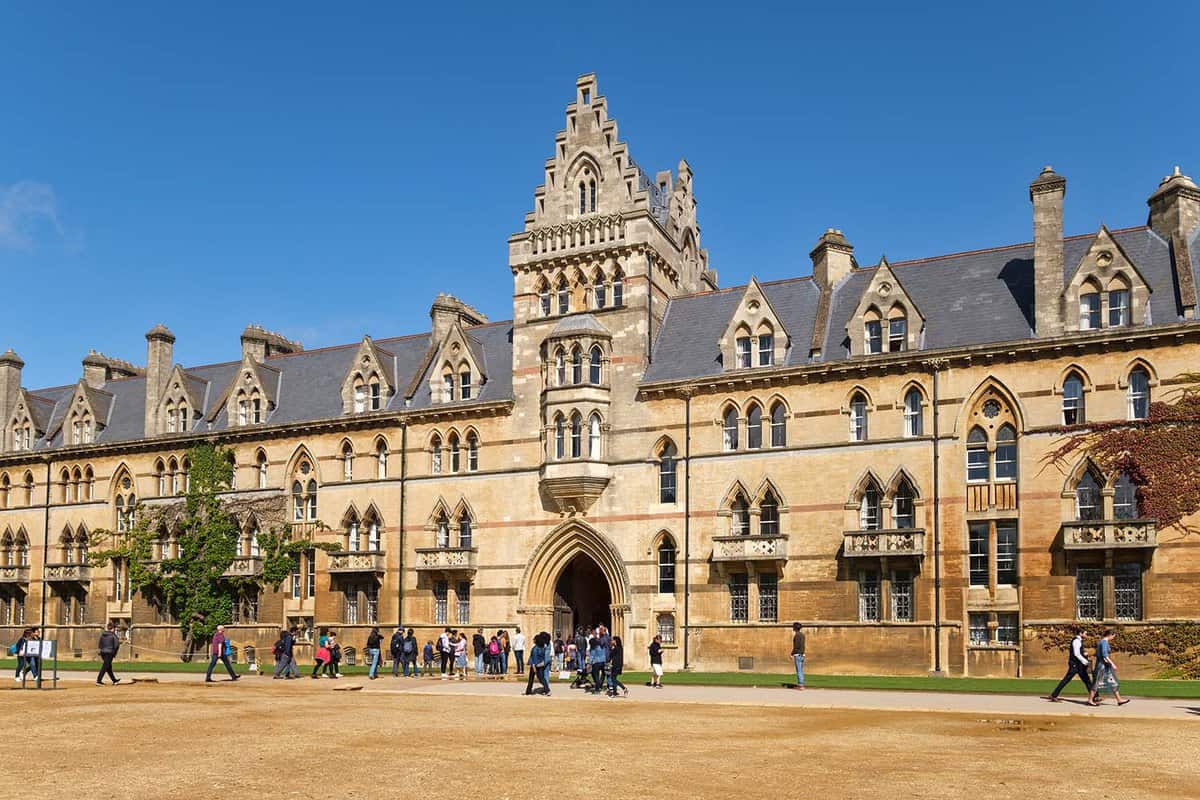 Students and families stand and walk in front of Christ Church College's sandstone building.