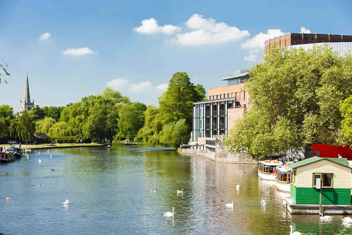 A far view of the Royal Shakespeare Company, showcasing the River Anon with a couple of swans swimming separately