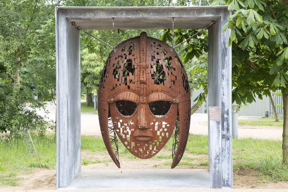 The iconic rust-coloured mask sculpture displayed in the woodlands