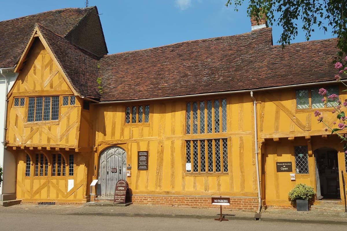 View of the remarkable yellow colored Little Hall in the charming village of Lavenham. The windows are portrait, rectangle shaped and the wooden door is shaped like an arch.