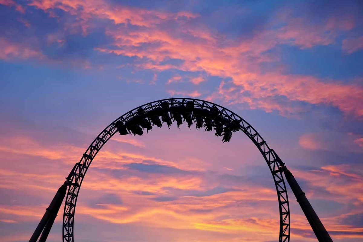Silhouette of people having fun on a roller-coaster in an amusement park at a golden pink and blue sunset