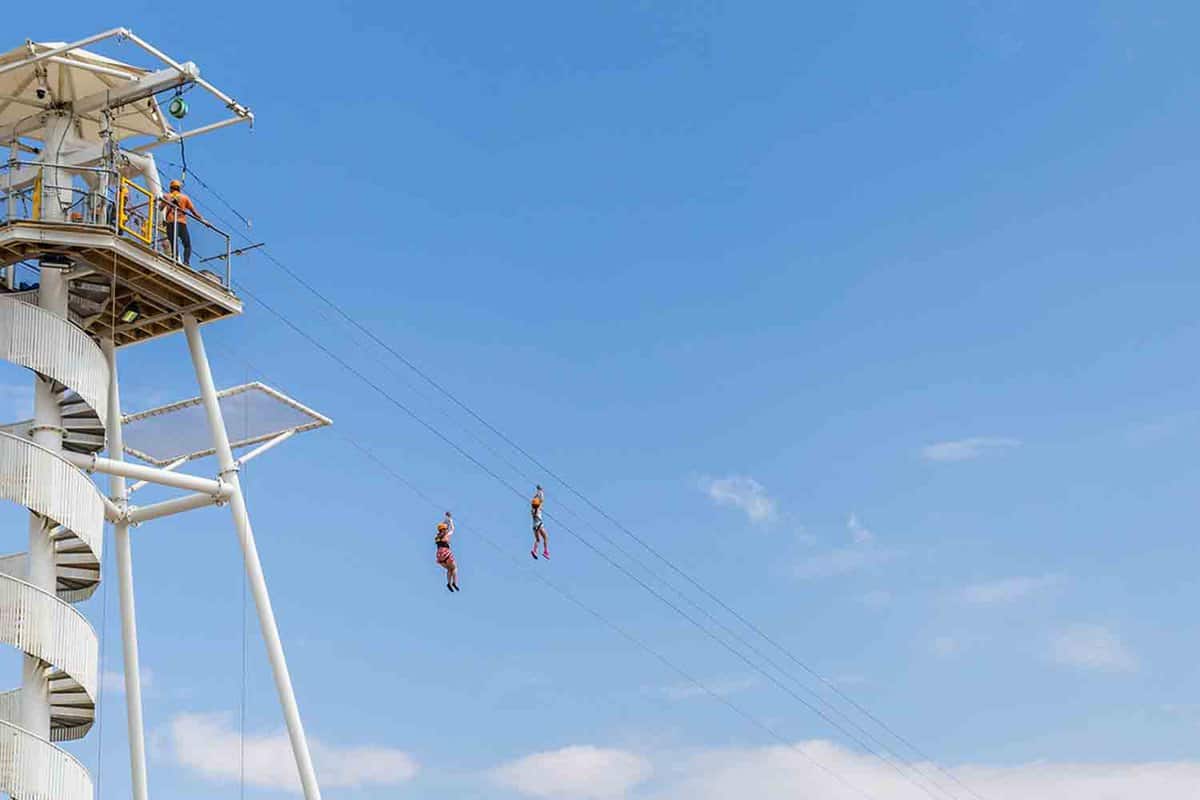 Two small figures ziplining from a high white tower.