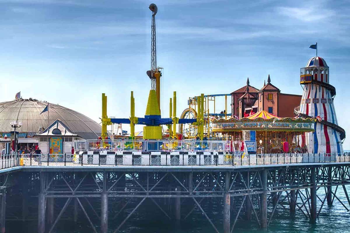 The fairground rides on Brighton pier. Painted in bright colours, the rides jut up into the blue sky. You can see the pier supports going down into the blue sea.