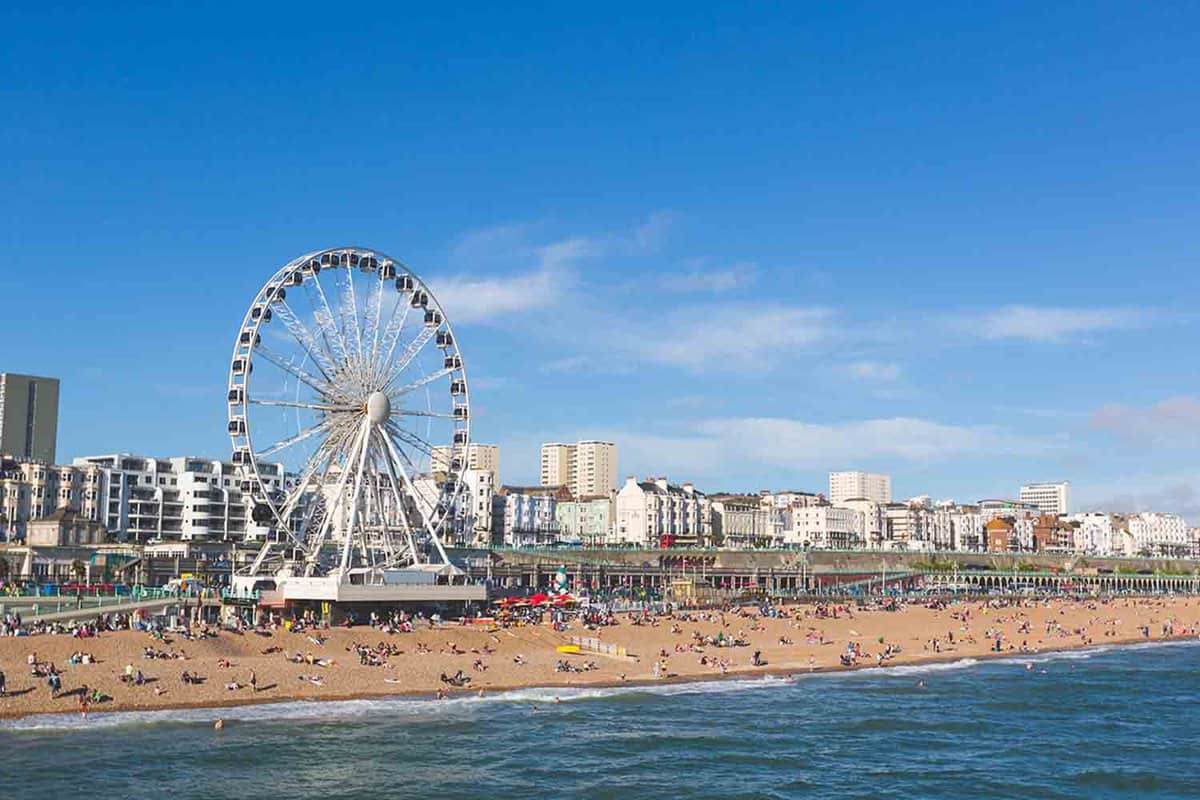 Brighton view of seaside from the pier. Panoramic shot with the famous ferris wheel, the stones beach with unrecognizable persons on a sunny summer day.