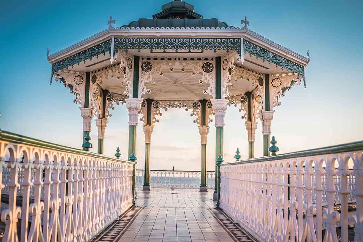 An empty bandstand in Brighton, painted in white and green. The sea peeks over the railings in the background.