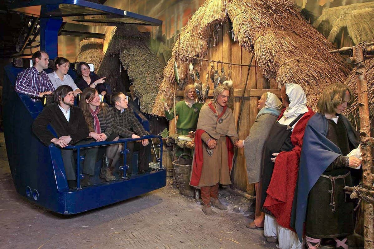 Visitors at a museum looking at mannequins in front a thatched-roof cottage