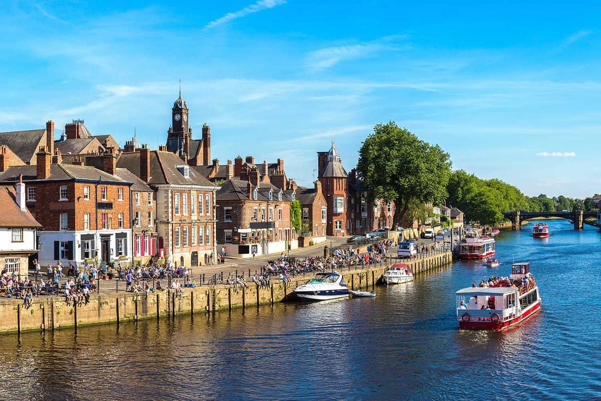 Boats sailing down the River Ouse with people walking along the embankment