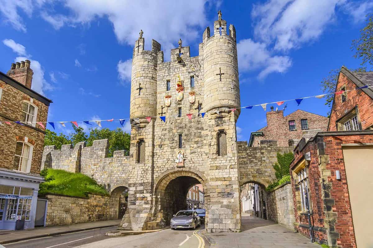 Car driving beneath medieval gate on ancient street with bunting strung across the road