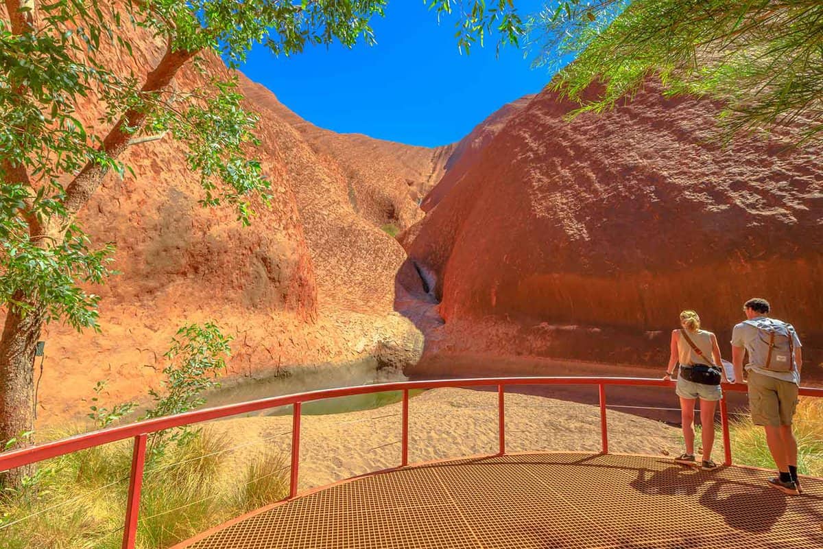 couple looking at waterhole in front of red rocks.
