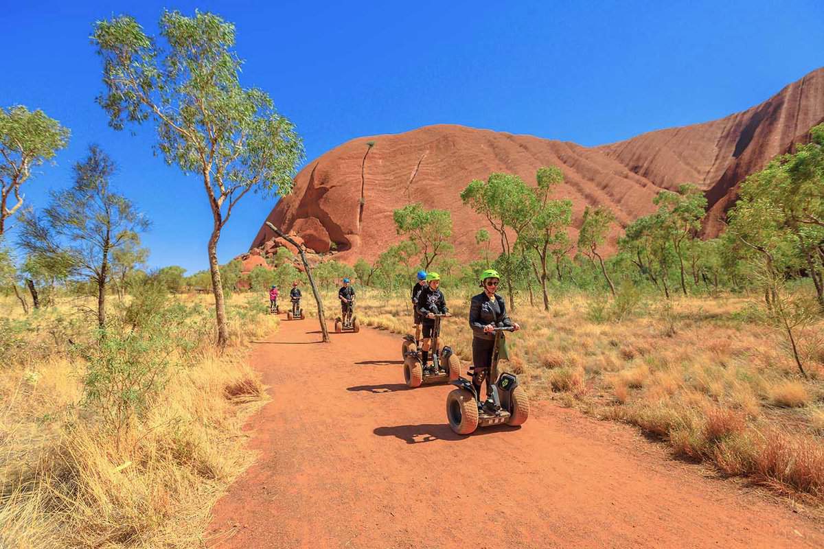 People segwaying on a pathway at the bottom of a red mountain.