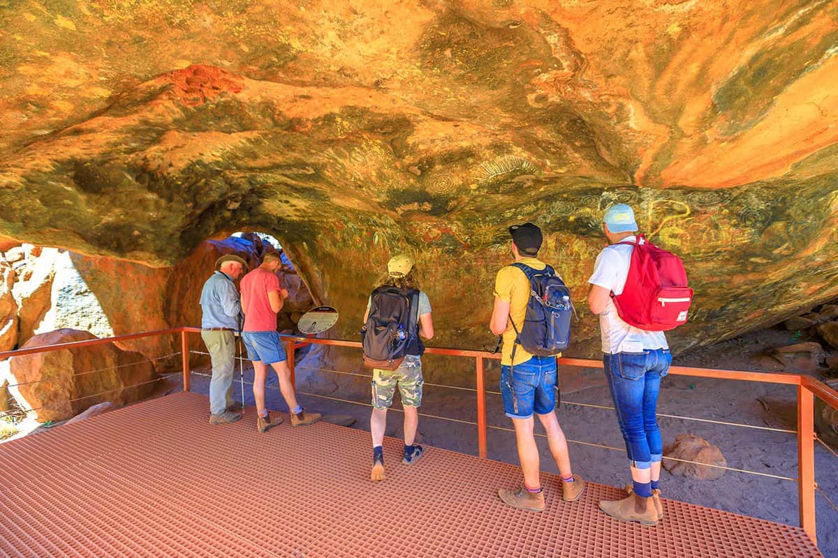 tourists looking drawings painted on rock in Mutitjulu Cave along Kuniya walk
