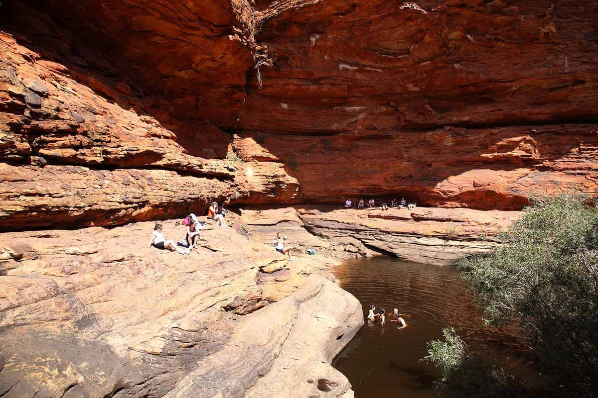 Tourists sitting and swimming in water in a large rock formation.