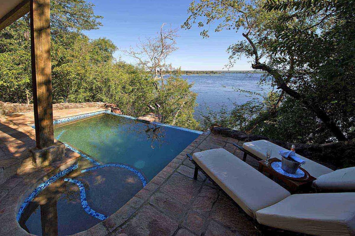 An outdoor pool with sun loungers looking out across water