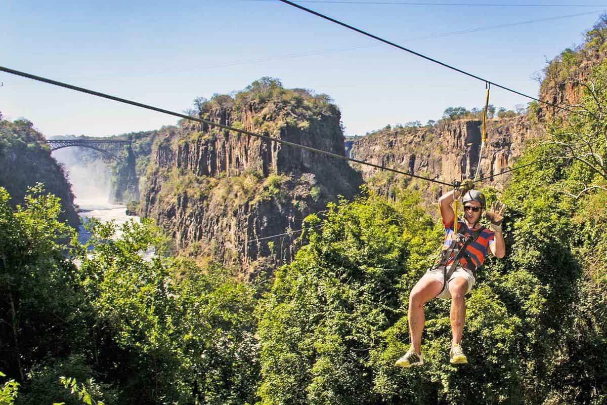 Man smiling on zip-line across the Zambezi with the Victoria Falls Waterfall in the backdrop