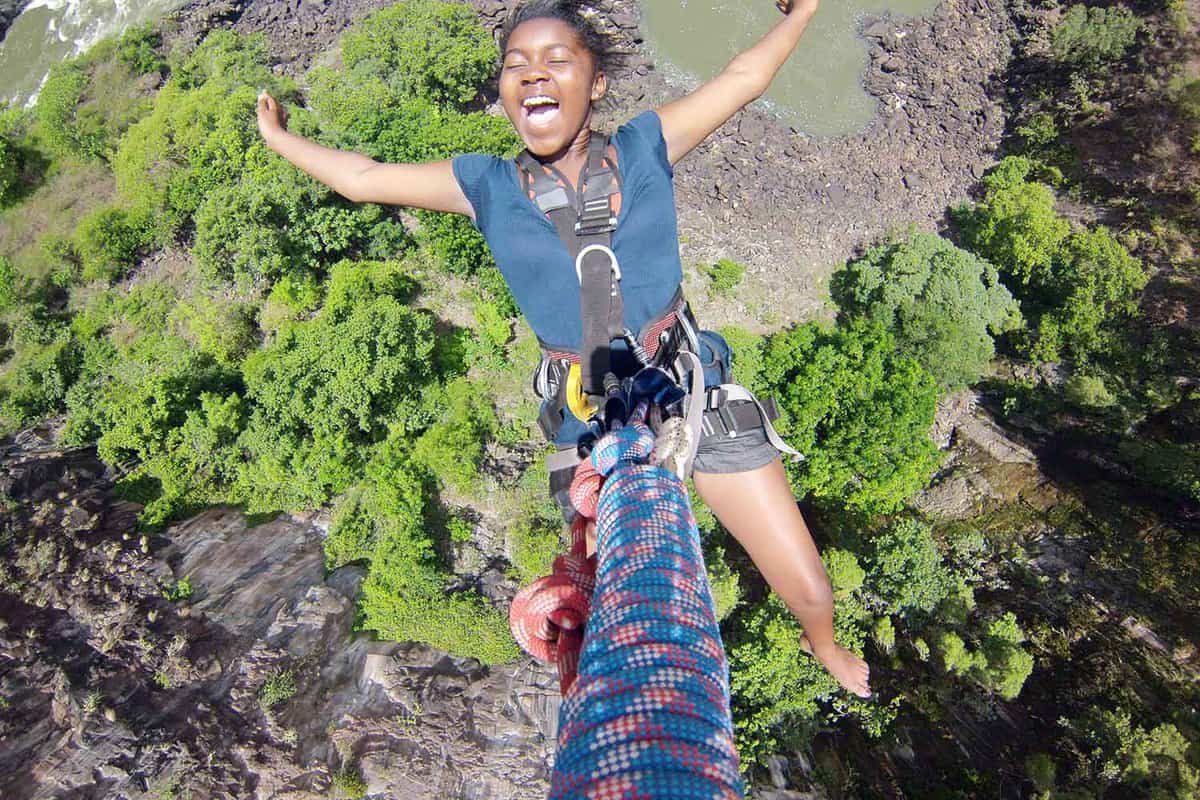 An aerial and selfie combined shot of a girl with her arms widespread on the zip-line with the Zambezi below
