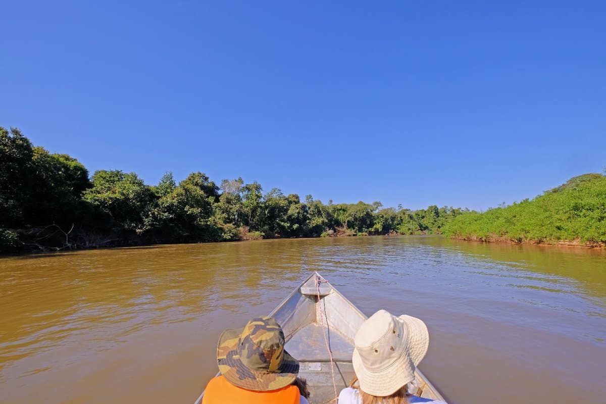 two tourists sitting at front of a canoe going along the river