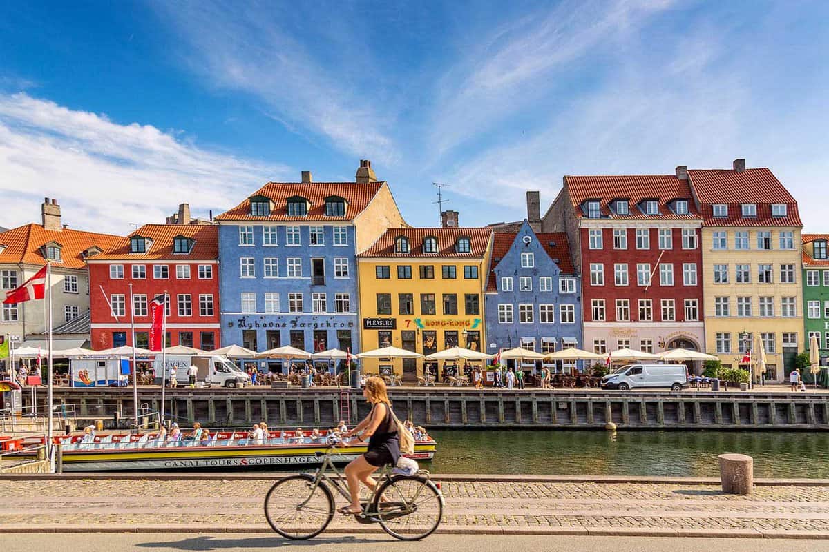 girl cycling along the Nyhavn canal with colourful buildings behind
