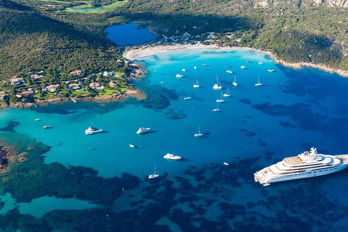 View from above, stunning aerial view of the Grande Pevero beach with boats and luxury yachts sailing on a turquoise, clear water. Sardinia