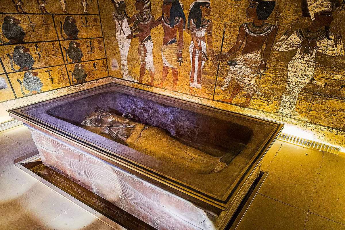 mummy on a glass box in a small room, walls covered in hieroglyphs