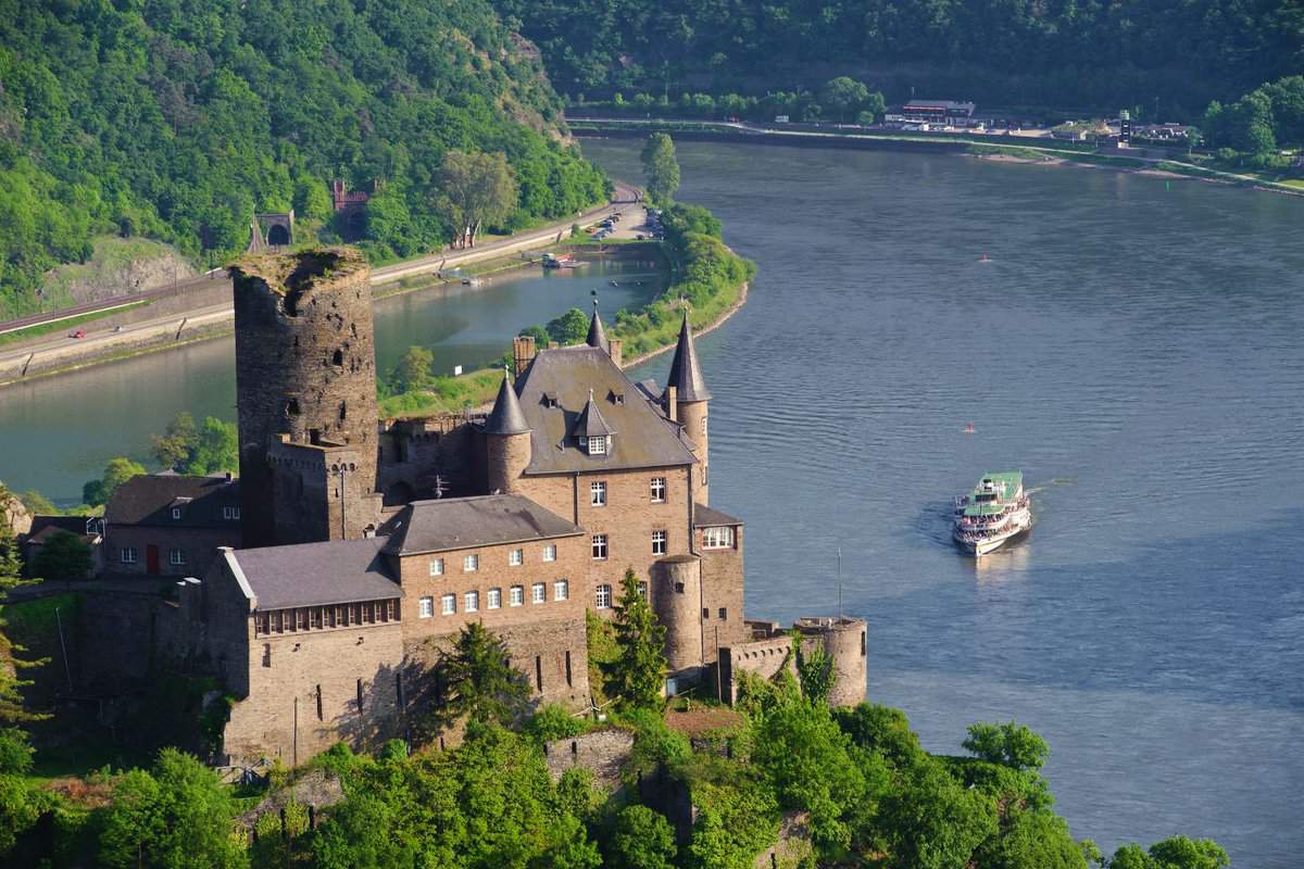large castle on a hill with river and cruise boat behind