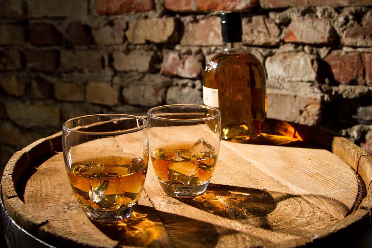 two small glasses of whiskey with bottle behind in a distillery