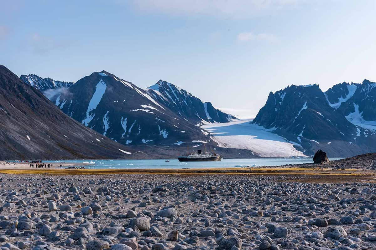 tiny cruise ship sailing before a large glacier and mountains