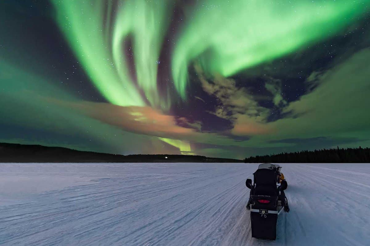 a snowmobile on white plain with northern lights in the sky above