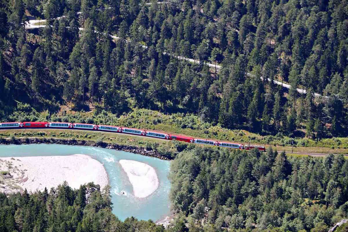 Aerial view down on famous red train Glacier Express drives alongside river Rhine in canyon